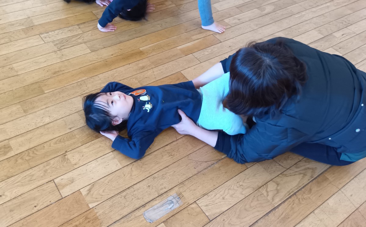 ブリッジをする子どもと、それを手伝うスタッフの様子