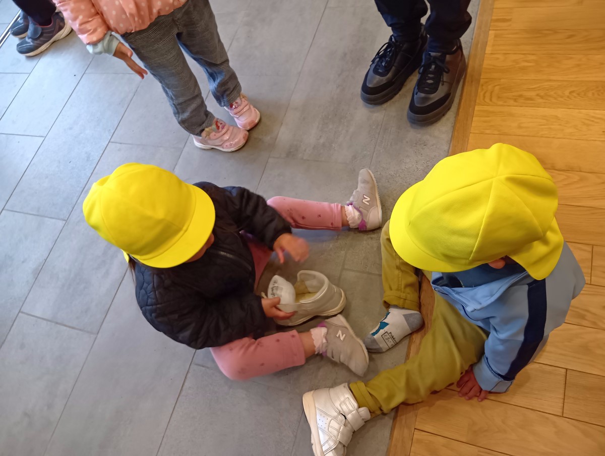 友達が靴を履くのを手伝う子ども