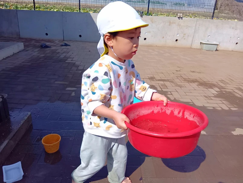 たらいに水を入れて運ぶ子ども