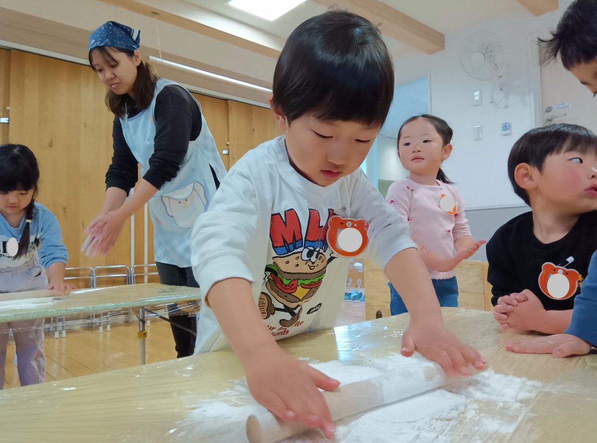 麺棒を使って生地をのばしていく子ども