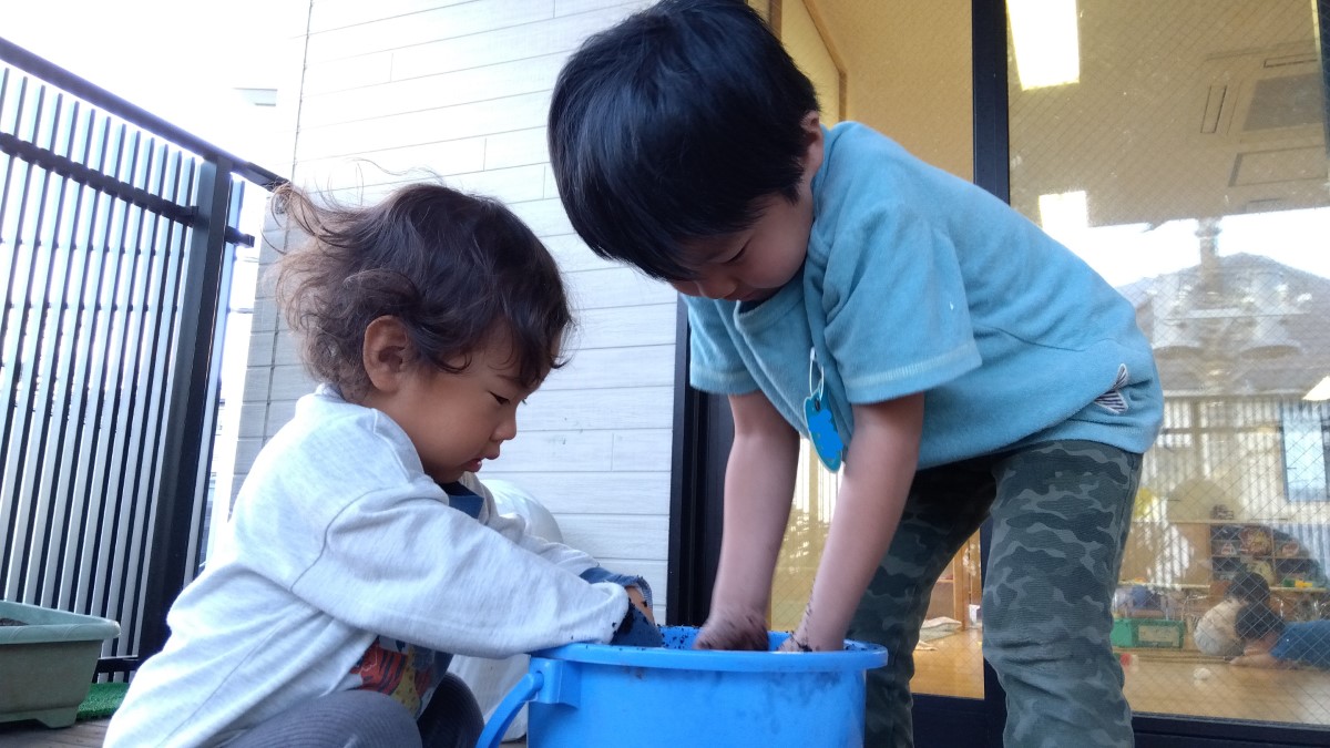 乳児と幼児で一緒に泥遊びをする様子