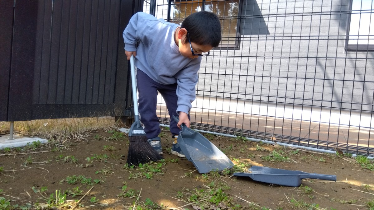 ほうきとちりとりでヤギ掃除をする子ども