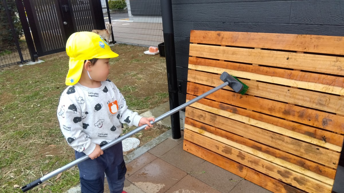 すのこをデッキブラシでこする子ども