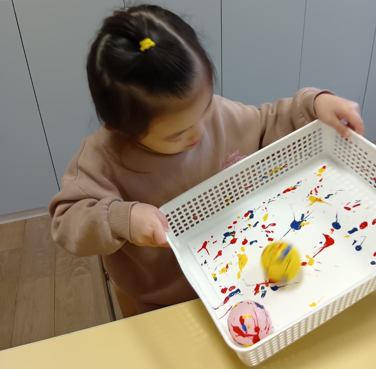 女の子が、絵具の上にボールを転がし、できる模様を楽しんでいる