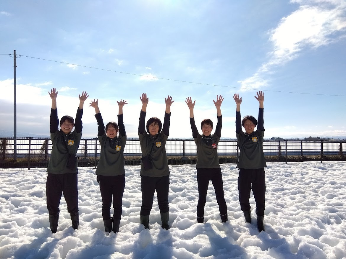 雪が積もる園庭にスタッフが5人並んでいる