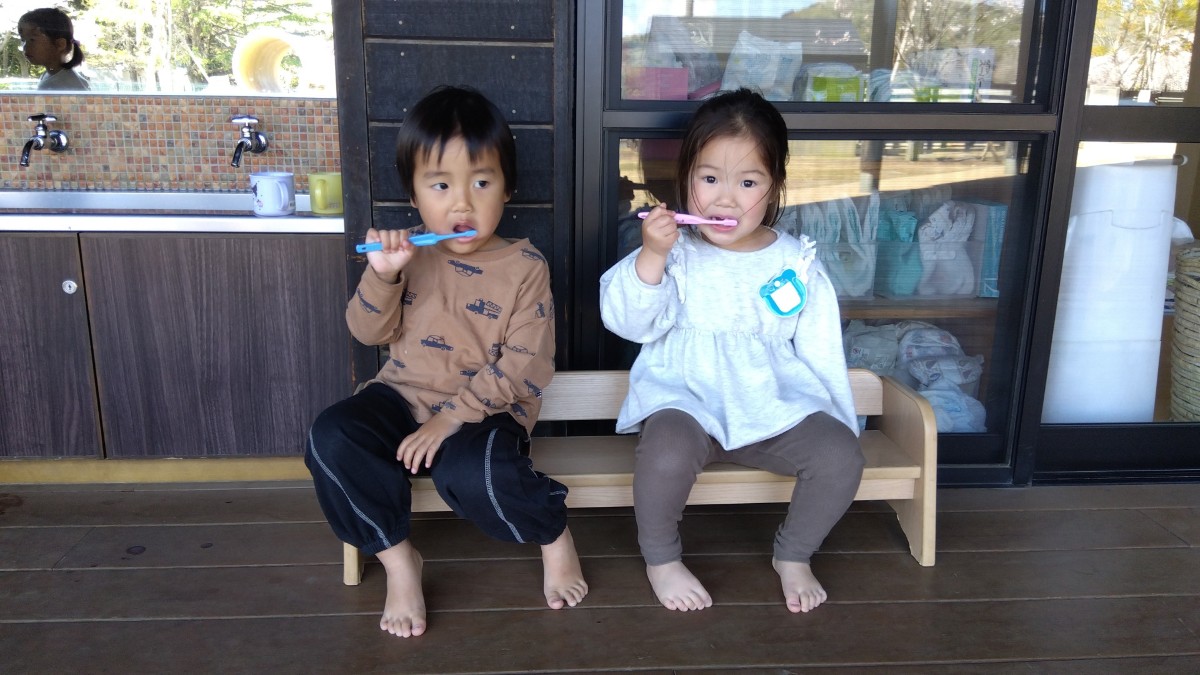 子どもが二人並んで椅子にすわり、歯磨きをしている