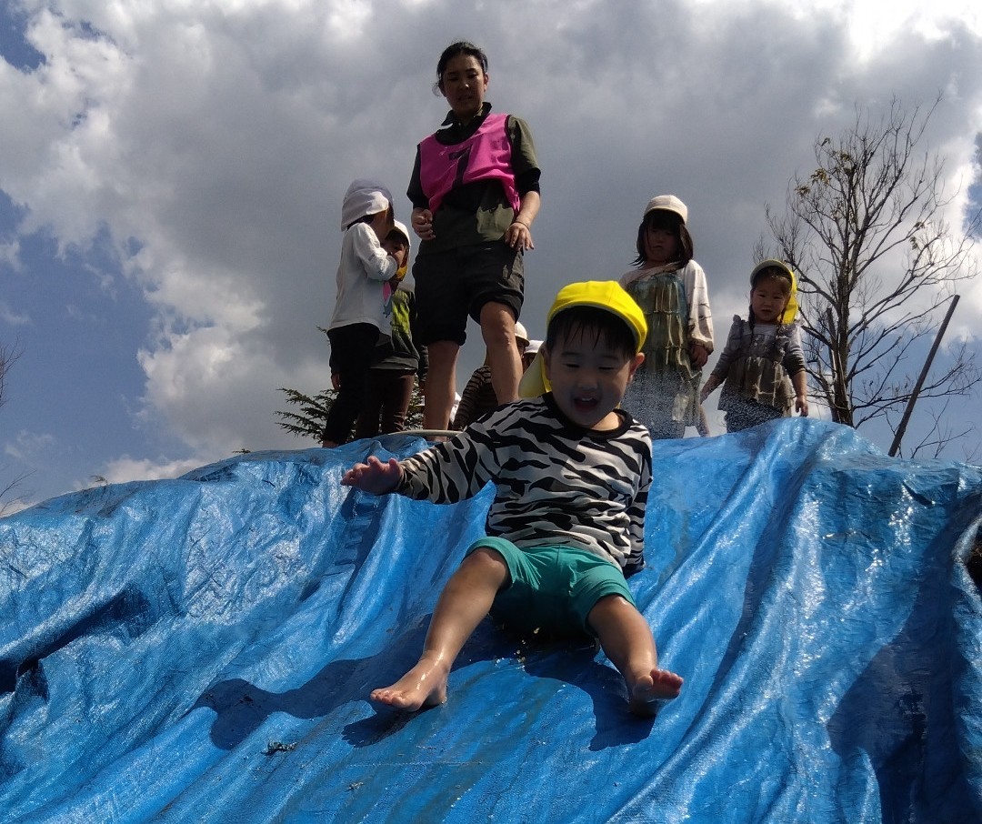 子どもたちが順番に築山から泥スライダーを滑り降りている