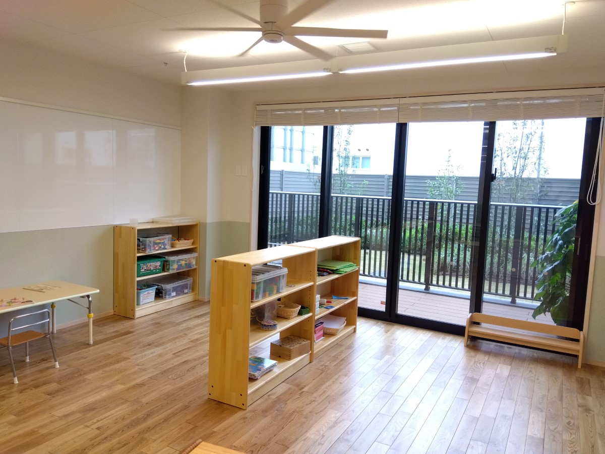 窓のそばにブロックなどを収納した棚が置かれている保育室内