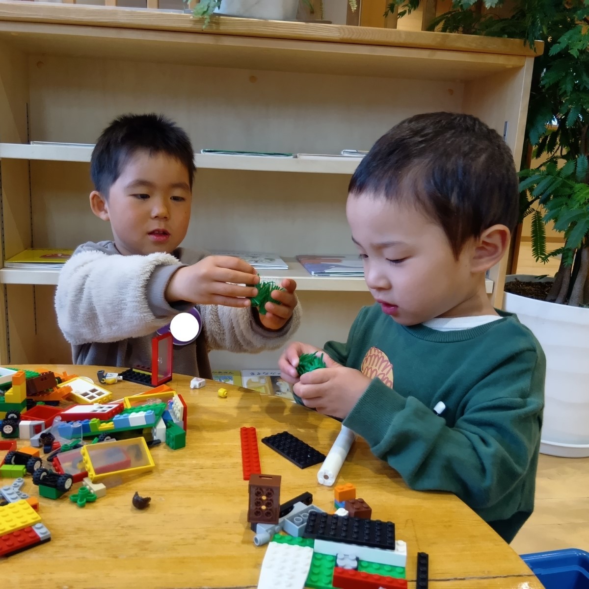ブロック遊びをしていた二人の男の子のうちの一人が、使っていたブロックを隣の友達に渡して言葉を交わしている