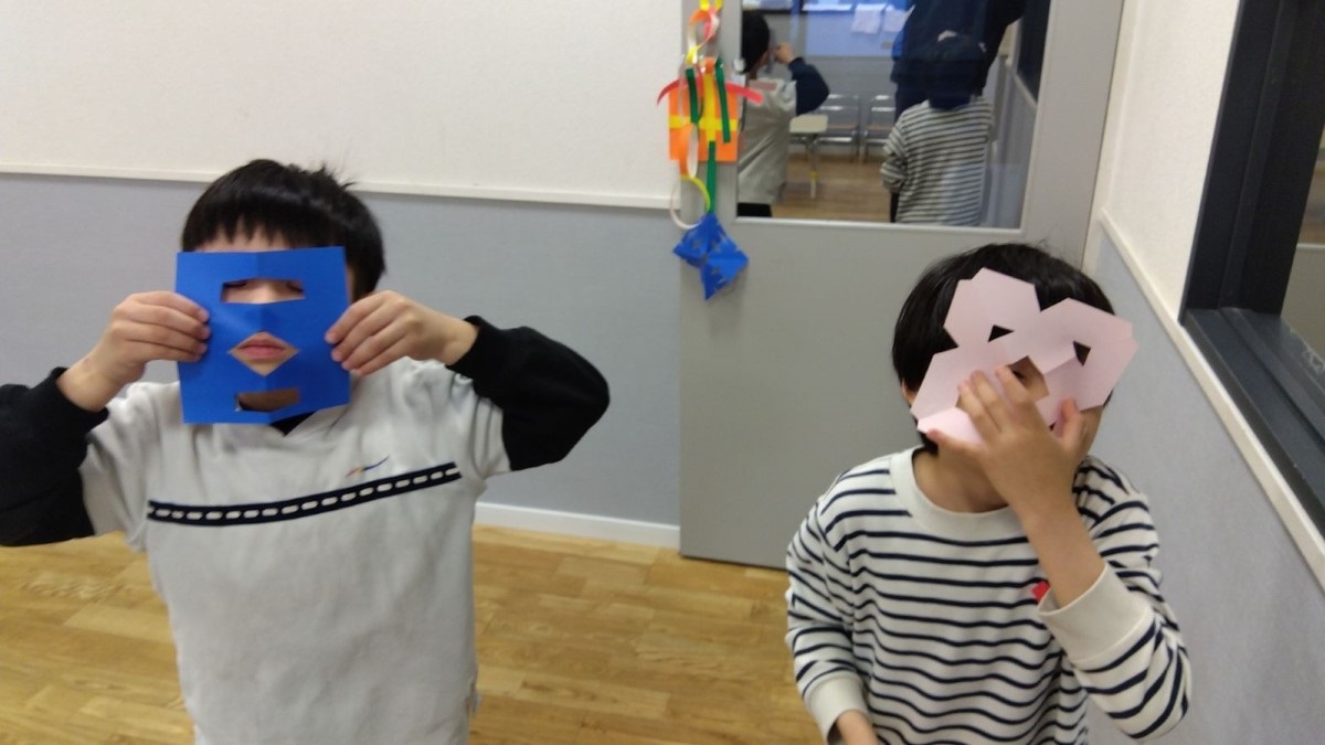 折り紙を顔に当ててみせる子どもたち