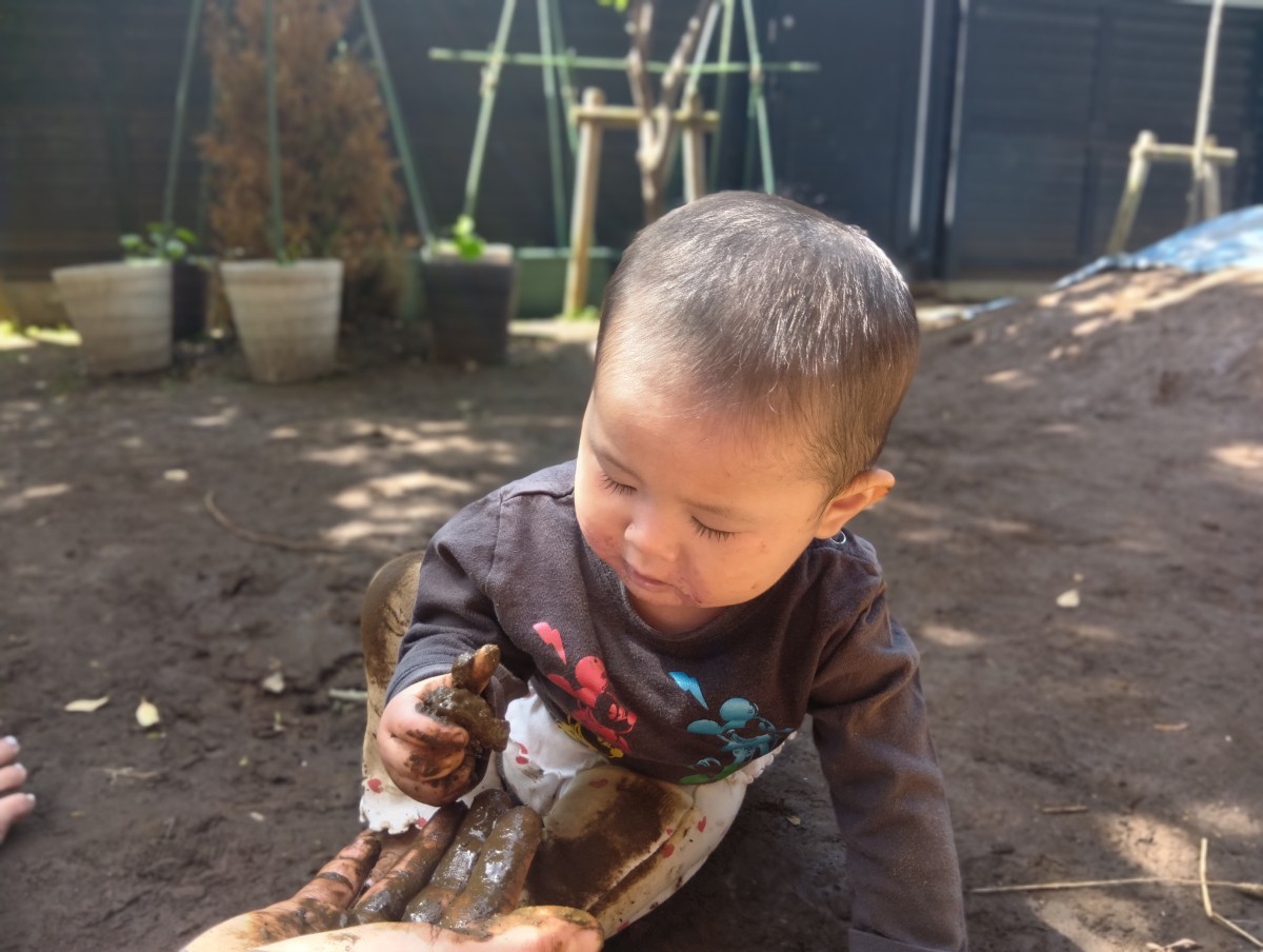 保育者から手渡しされてた泥団子に手を伸ばして握っている子ども