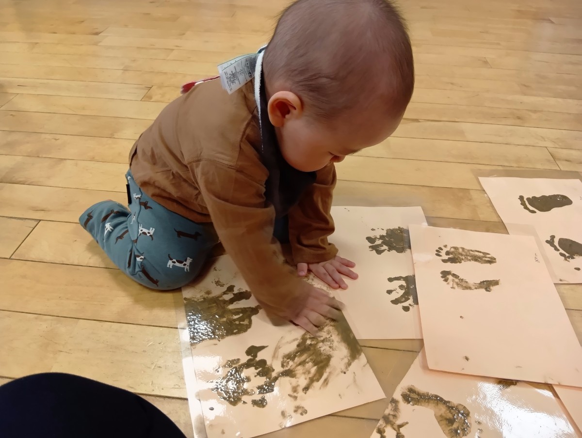 子どもが画用紙に描いた泥の手形に触れている