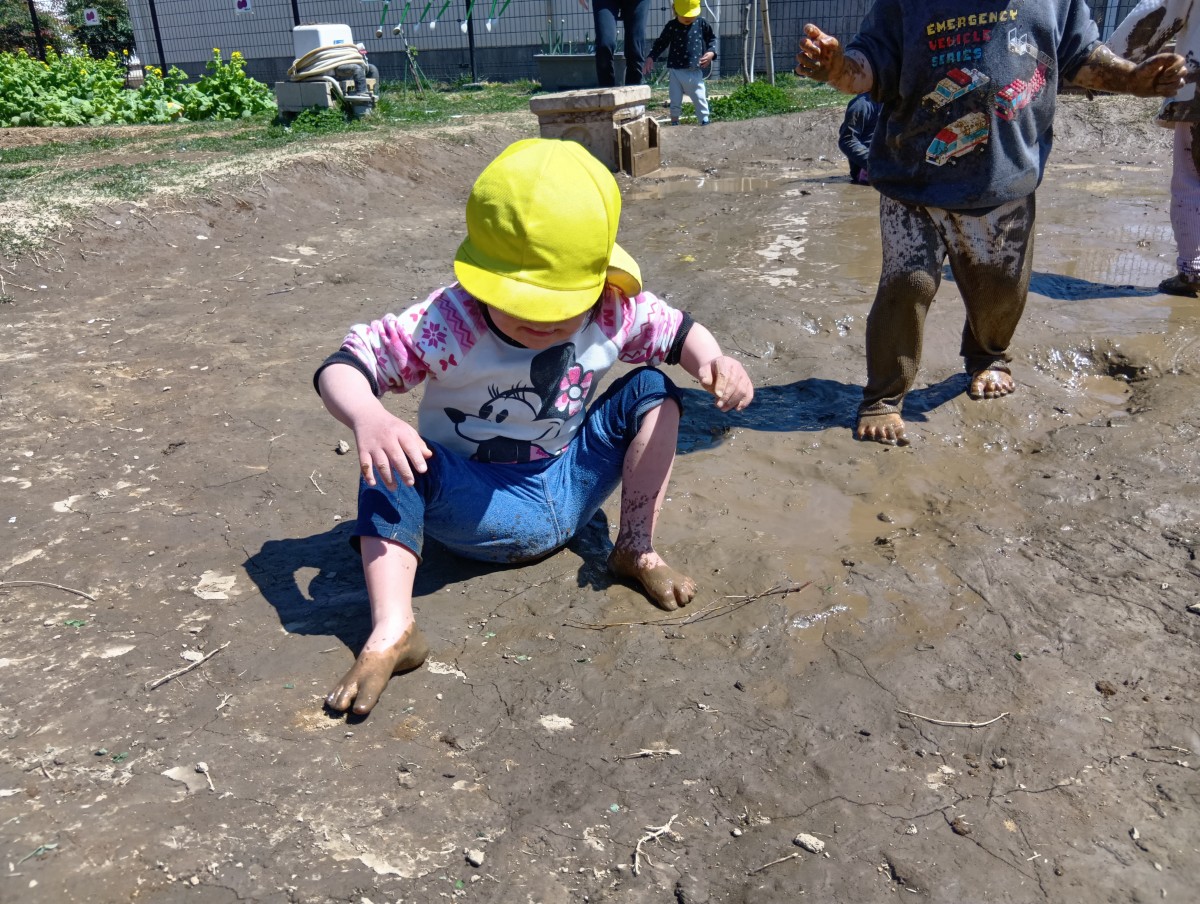 泥の上で歩いたりしゃがんだりしている子どもたち