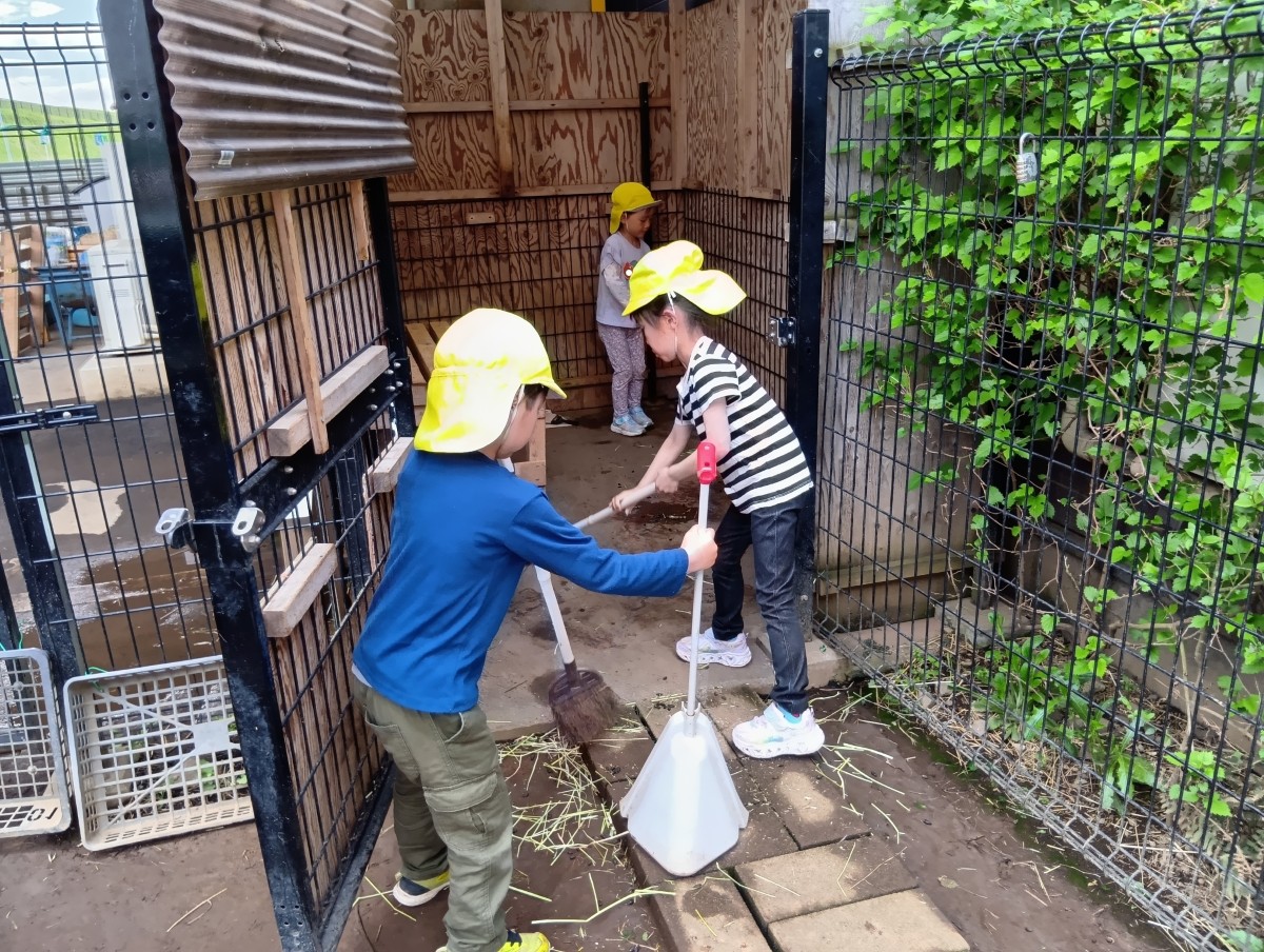 三人の子どもたちが塵取りや箒を手に持ち、小屋を掃除している