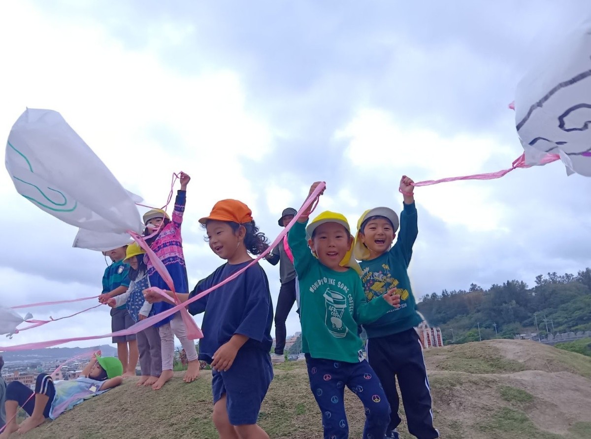 子どもたちが高山の上に立ち、自ら作ったビニール凧を手に持って腕をあげている