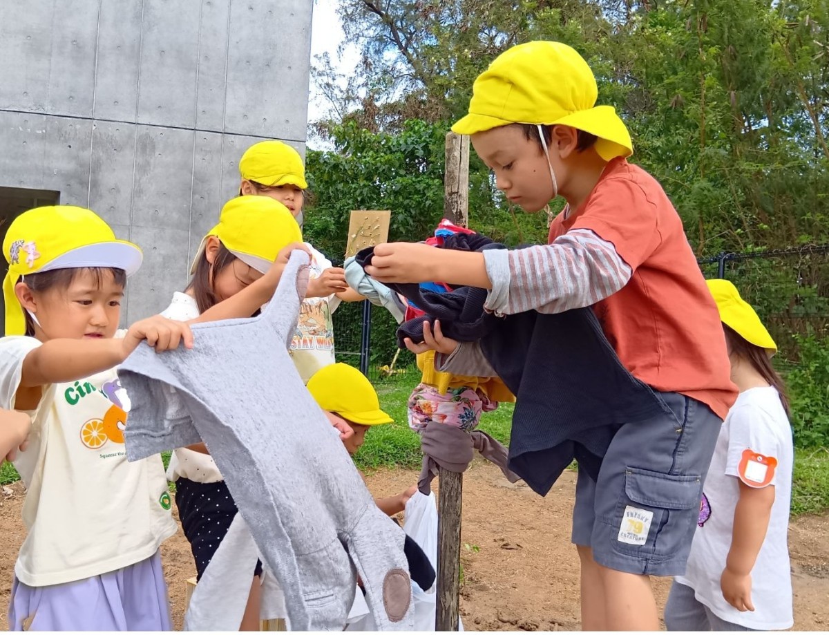 案山子の土台となる木の枝に洋服を着せようとする子、洋服を広げている子などがいる