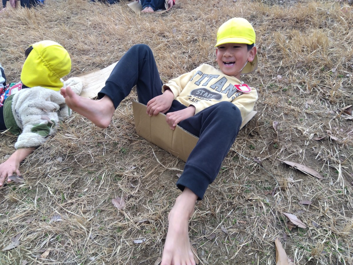 子どもが段ボールを使って芝滑りを楽しんでいる