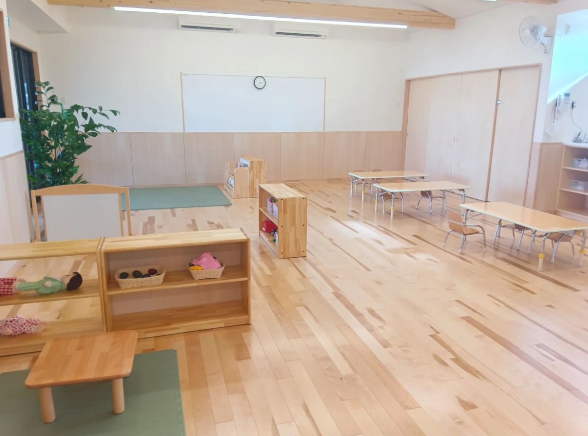保育室内は乳児用の机と椅子が並び、棚には絵本や人形、玩具が取り出しやすく置かれている
