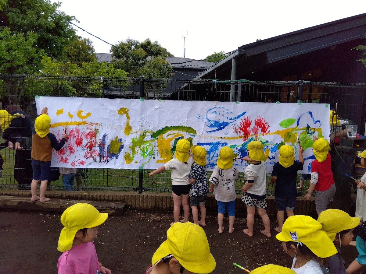 屋外の大きなキャンパスに絵を描く子どもたち