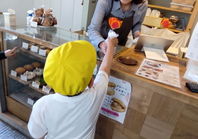 ドーナッツ屋の店員に子どもがチューリップの切り花を渡している。