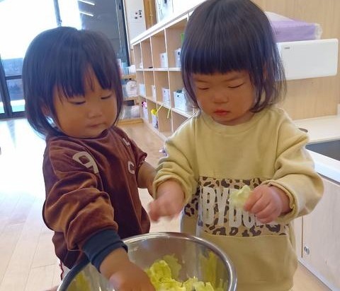 二人の子どもが、ボールに入ったキャベツをつまんでちぎっている。