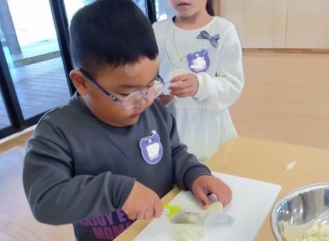 めがねをかけた子どもが、包丁で玉ねぎを薄く切っている。