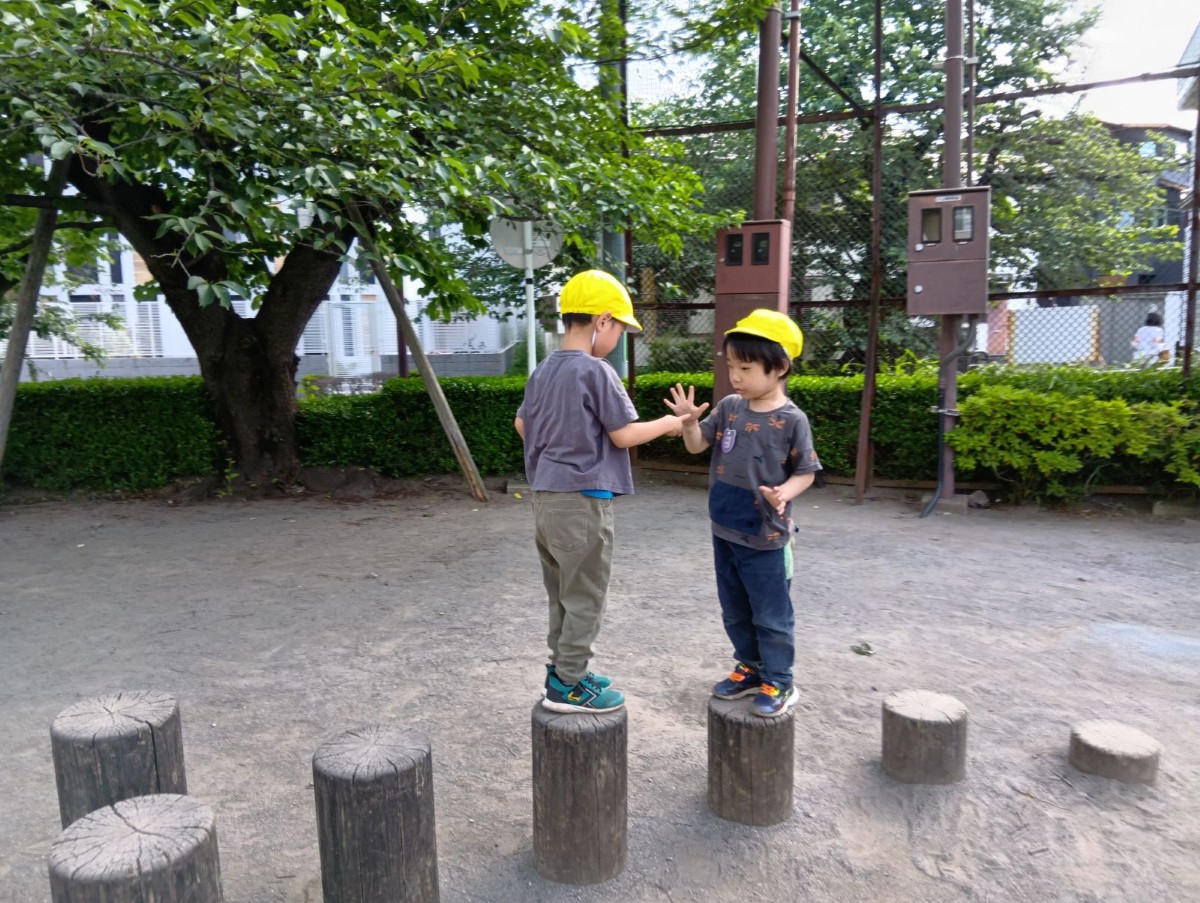 丸太の上を歩いて近づいた子どもたちが互いに向き合い、じゃんけんをしている。