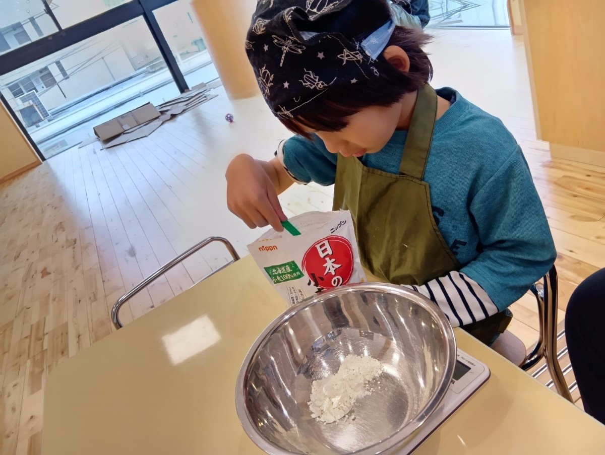 子どもが小麦粉をスプーンですくい、小麦粉の量を量っている。