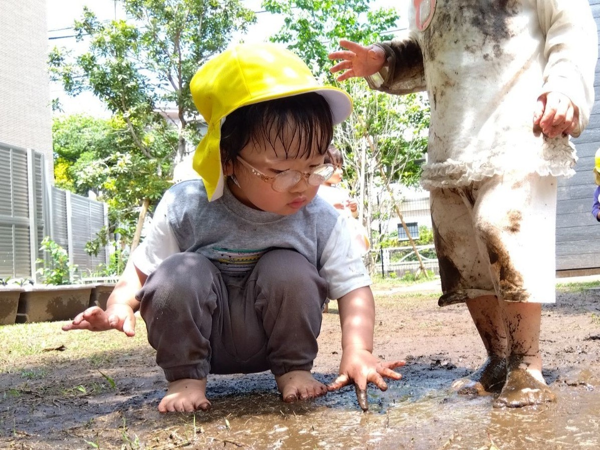 全身泥だらけになって立っている子どもと、そっと指先で泥に触れる子どもが並んでいる。