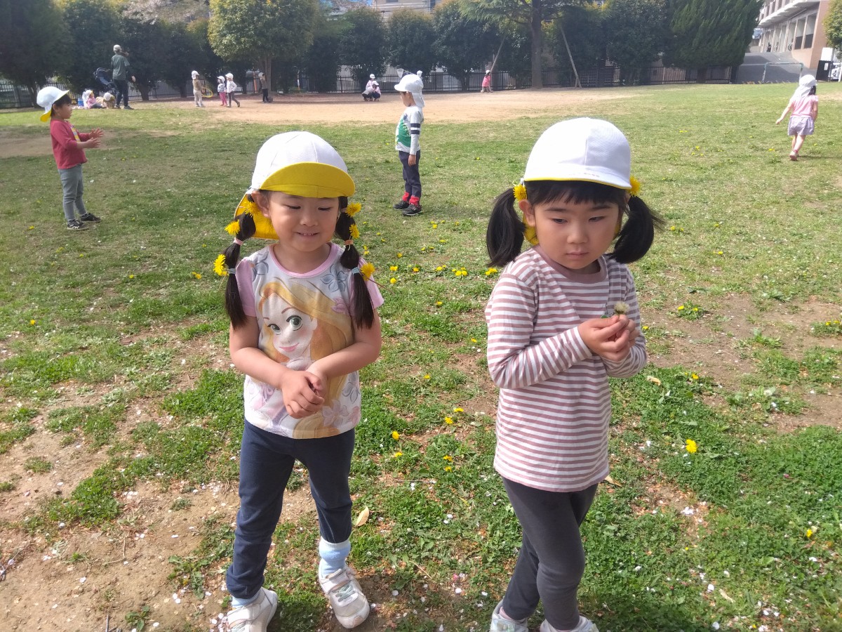 公園で見つけたタンポポを髪飾りにつけた二人の子どもが並んでいる。