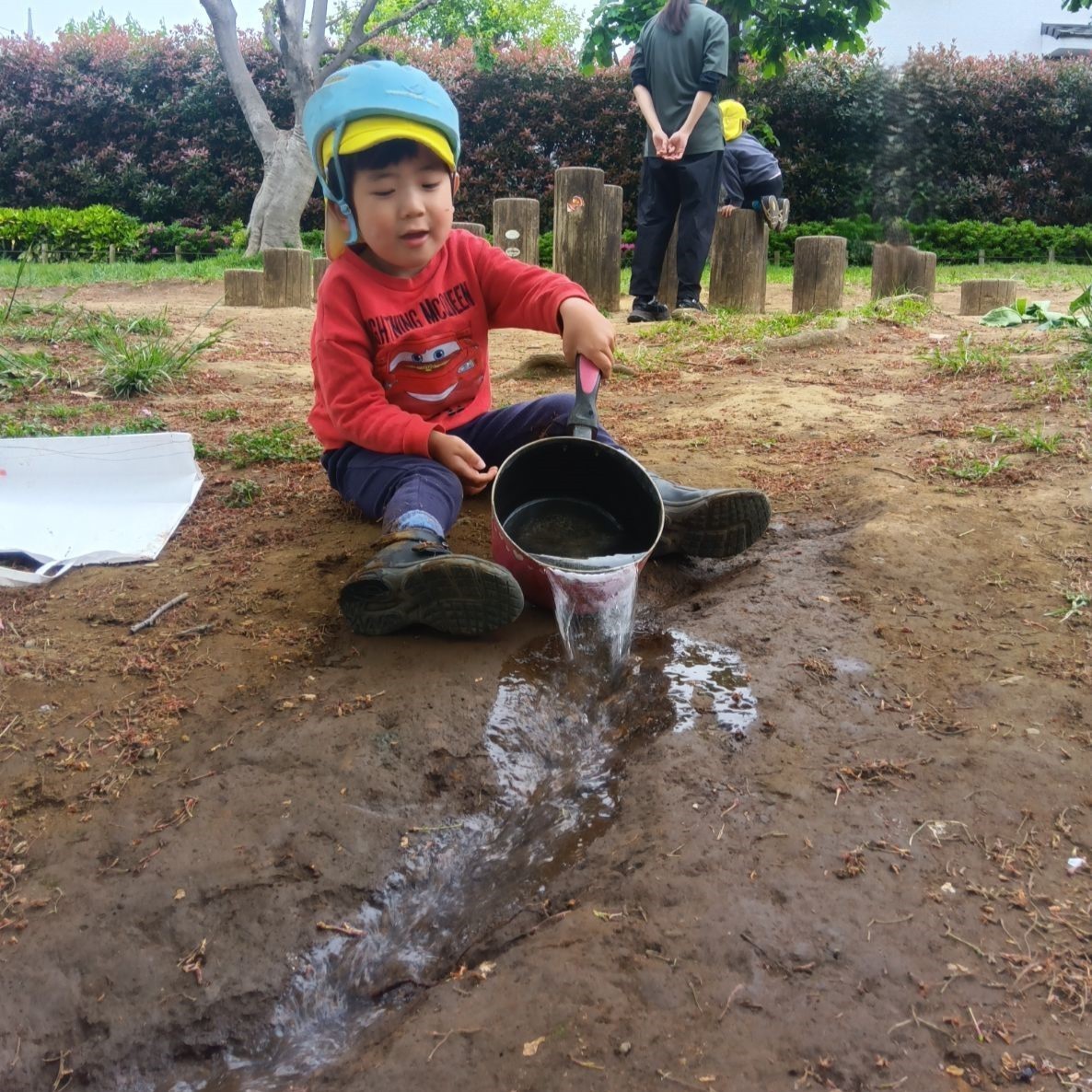 一人の子どもが、少しくぼんだ土の上からフライパンに入った水を流している。