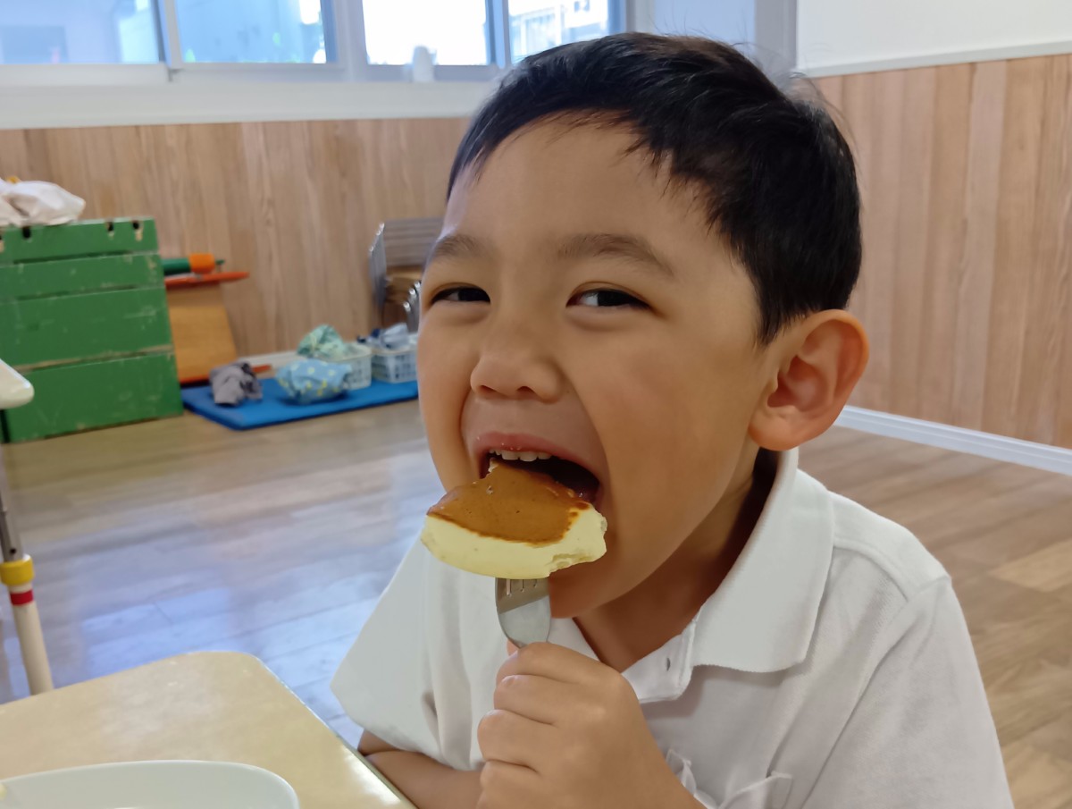 子どもがフォークにパンケーキを刺して、大きな口を開けて食べている。サムネイル