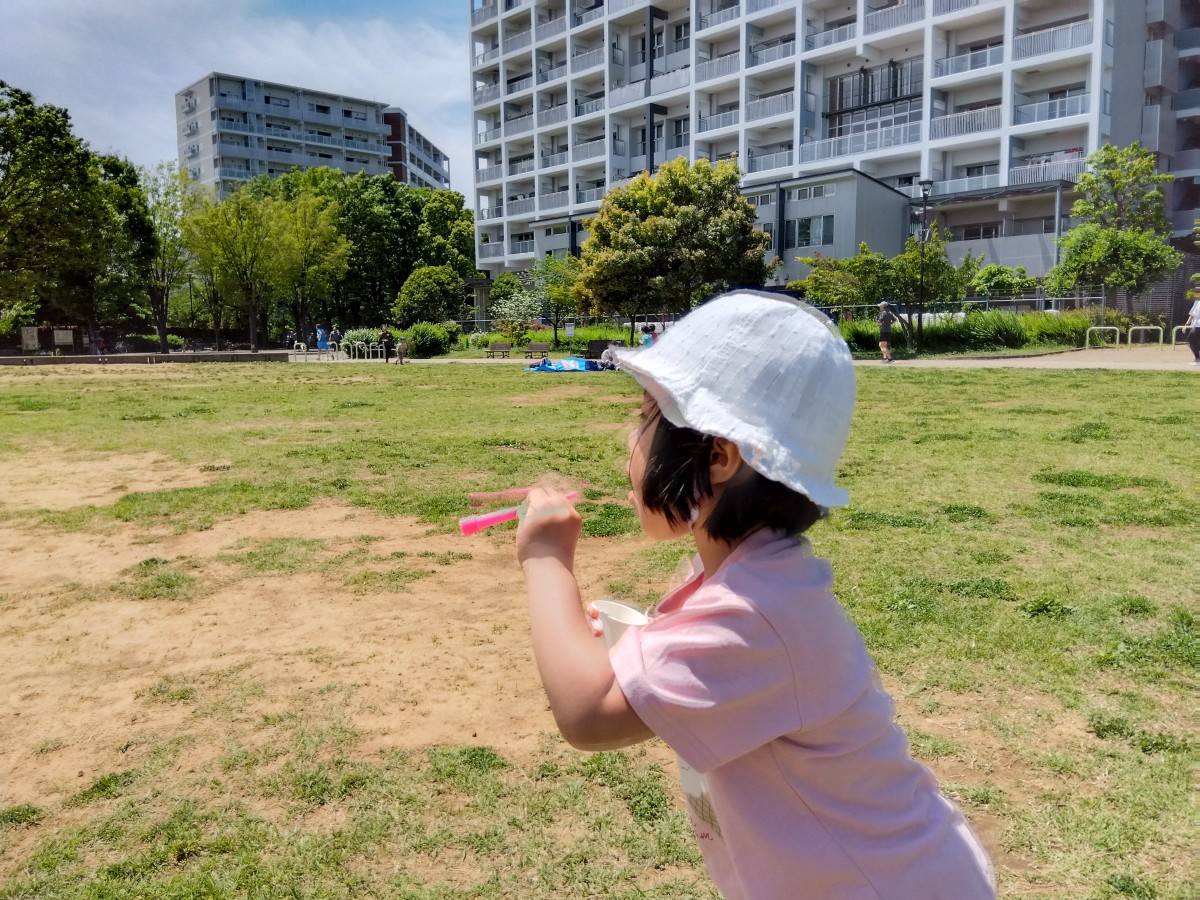 草原では、シャボン玉を吹こうとする帽子をかぶった子どもがいる。