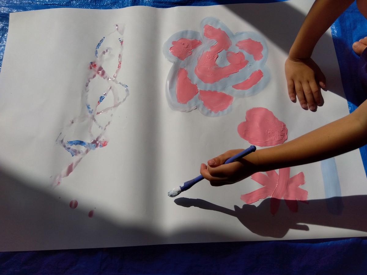 一人の子どもが筆を持ってしゃがみ、床に置かれた画用紙に絵を描いている。