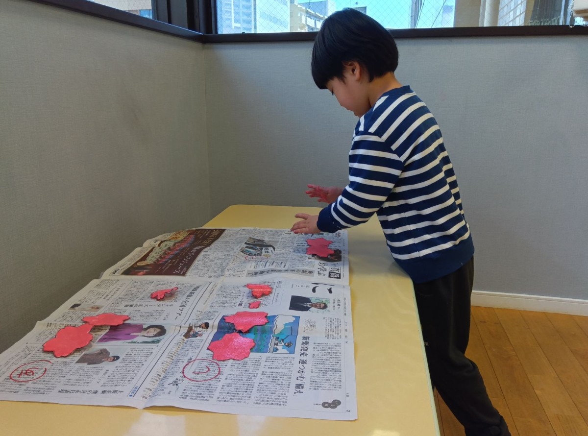 一人の子どもが自分で色付けをした画用紙の花を新聞紙の上に置いている。