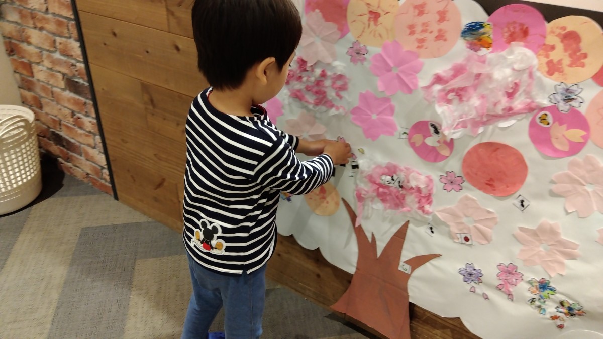 壁面に大きな画用紙の木が貼られており、そこに一人の子どもが制作した桜の花を貼り付けている。