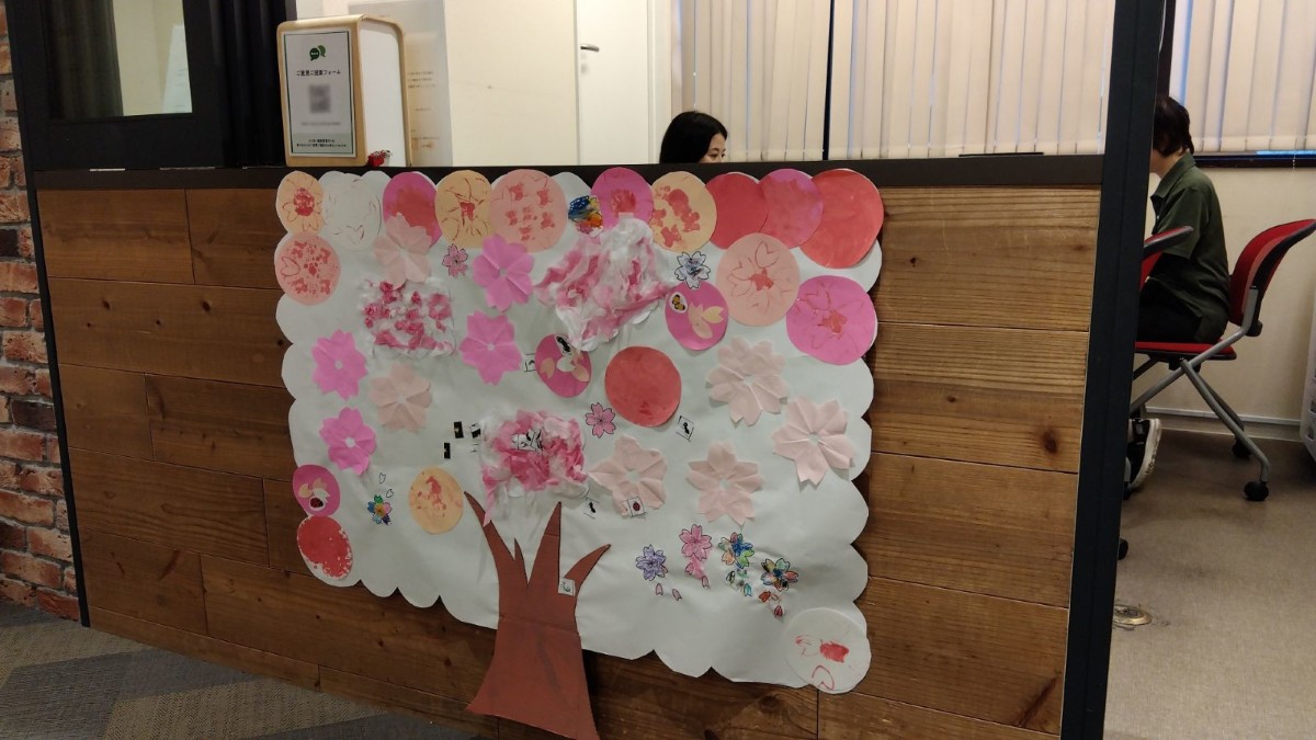 折り紙、切り紙、塗り絵、お絵かきなどで子どもたちが制作した桜の花や蝶や蟻が大きな壁面の木に貼られている。