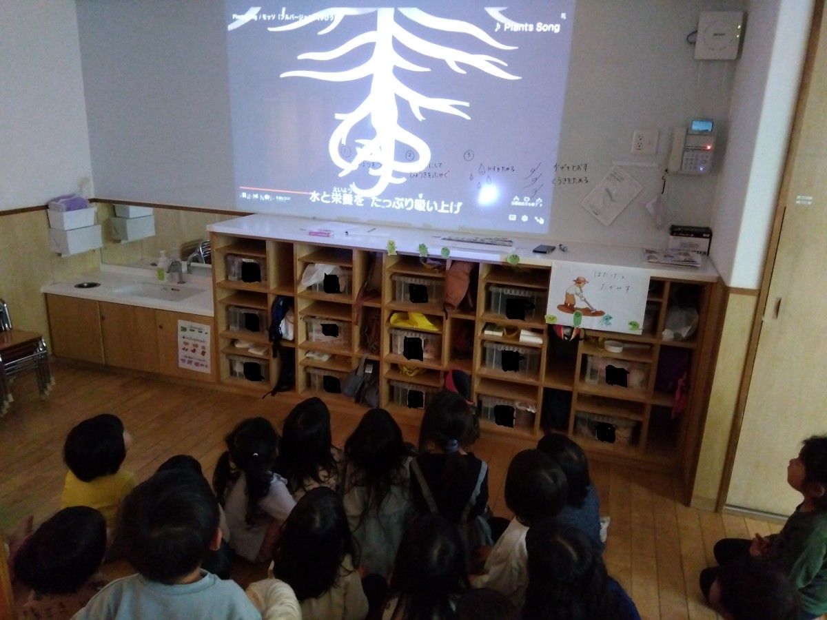 子どもたちはスクリーンに映し出された土の中の植物の映像を見ている。