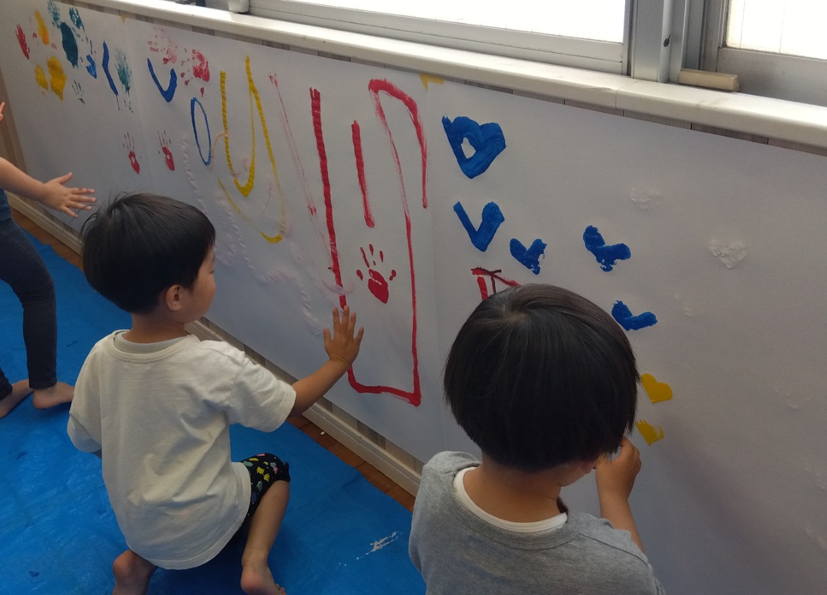 壁面に貼られた模造紙に、子どもたちが指や手を使って手形や模様を描いている。