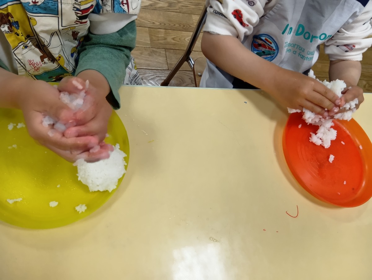 皿の上にご飯があり、子どもたちは両手でご飯をにぎっている。