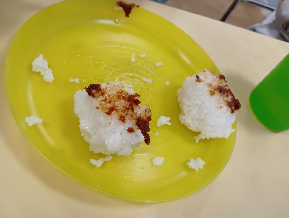 皿の上には、子どもが握った味噌がついたおにぎり２個と米粒が散在している。