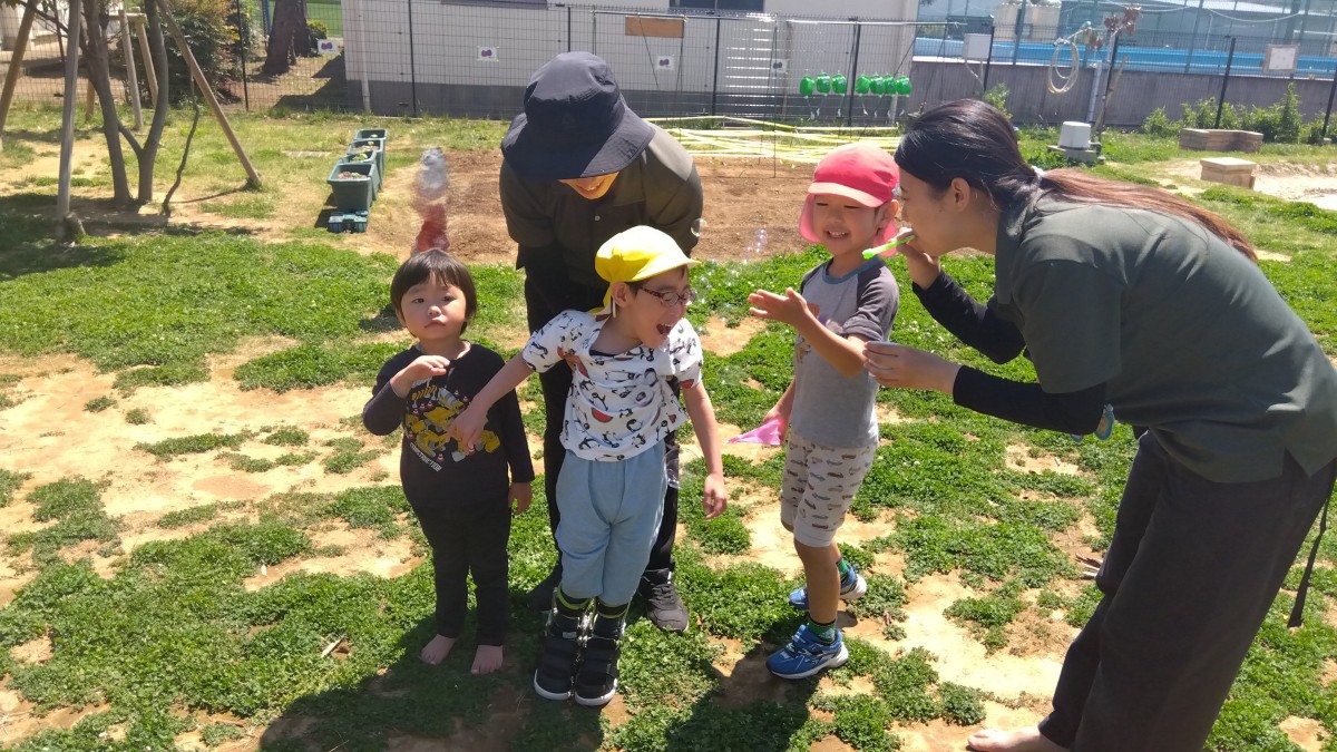 大人がシャボン玉を飛ばし、子どもたちが笑顔で喜んでいる。