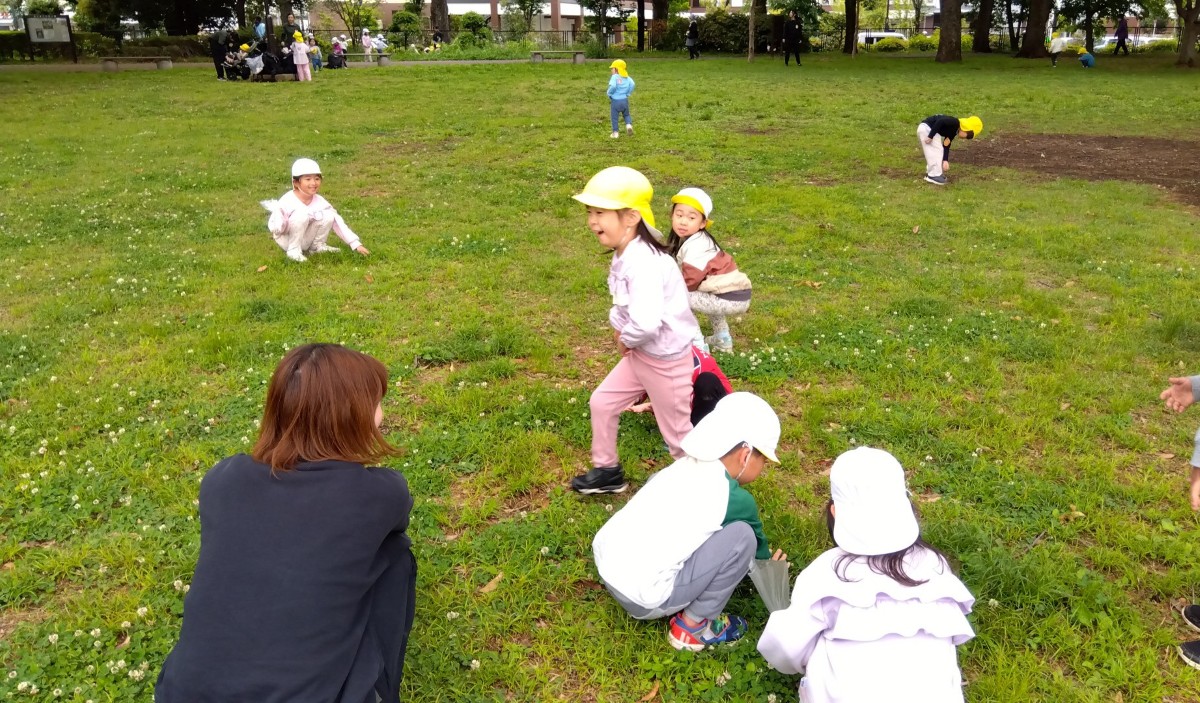 シロツメ草の原っぱで、子どもたちは走ったり歩いたりしゃがんで草を触ったりしている。