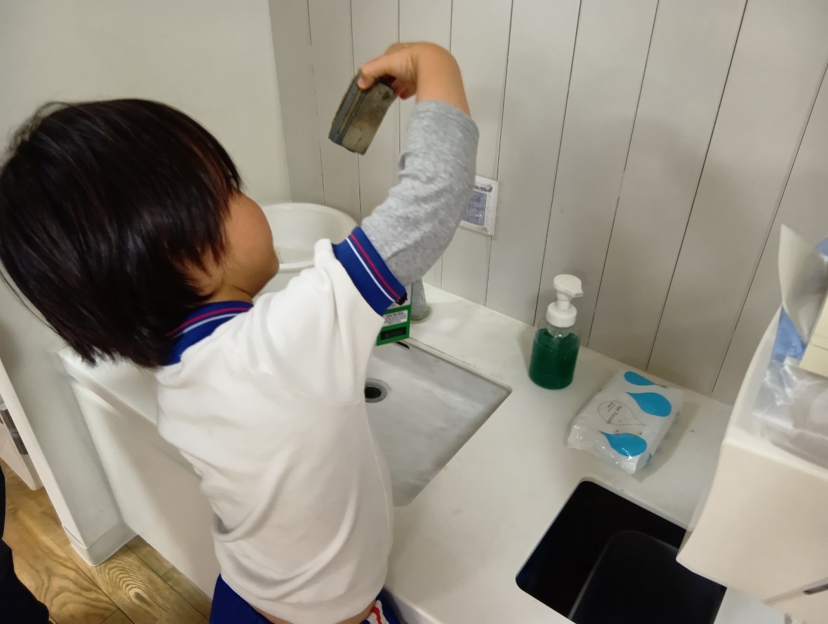 水道場では、一人の子どもが汚れたスポンジを手に持っている。