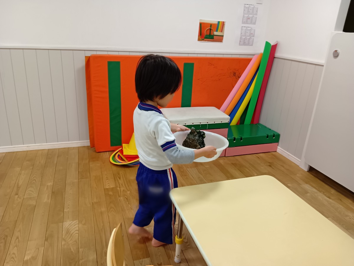一人の子どもが岩が入った桶を両手に持って運んでいる。