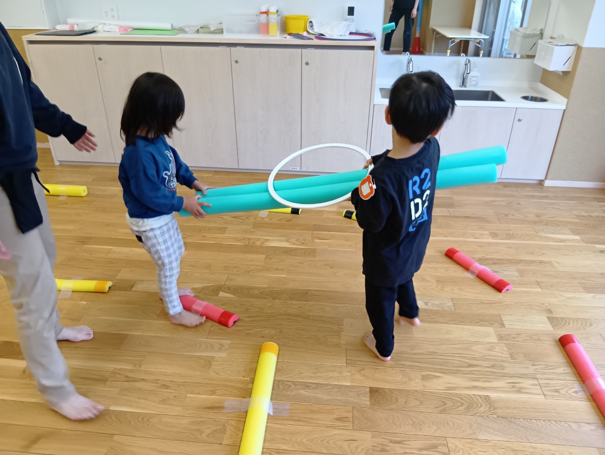 二人の子どもがスポンジ棒の両端を持ってサーキットのコースを歩いている。
