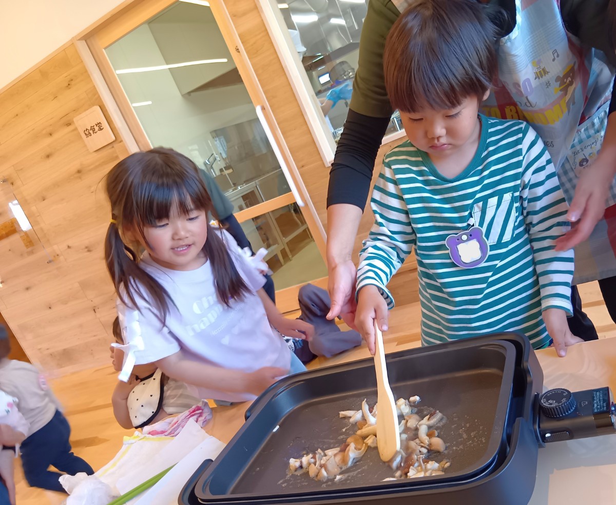 子どもが木べらを持ち、切ポットプレートの上で切られた椎茸を炒めている。