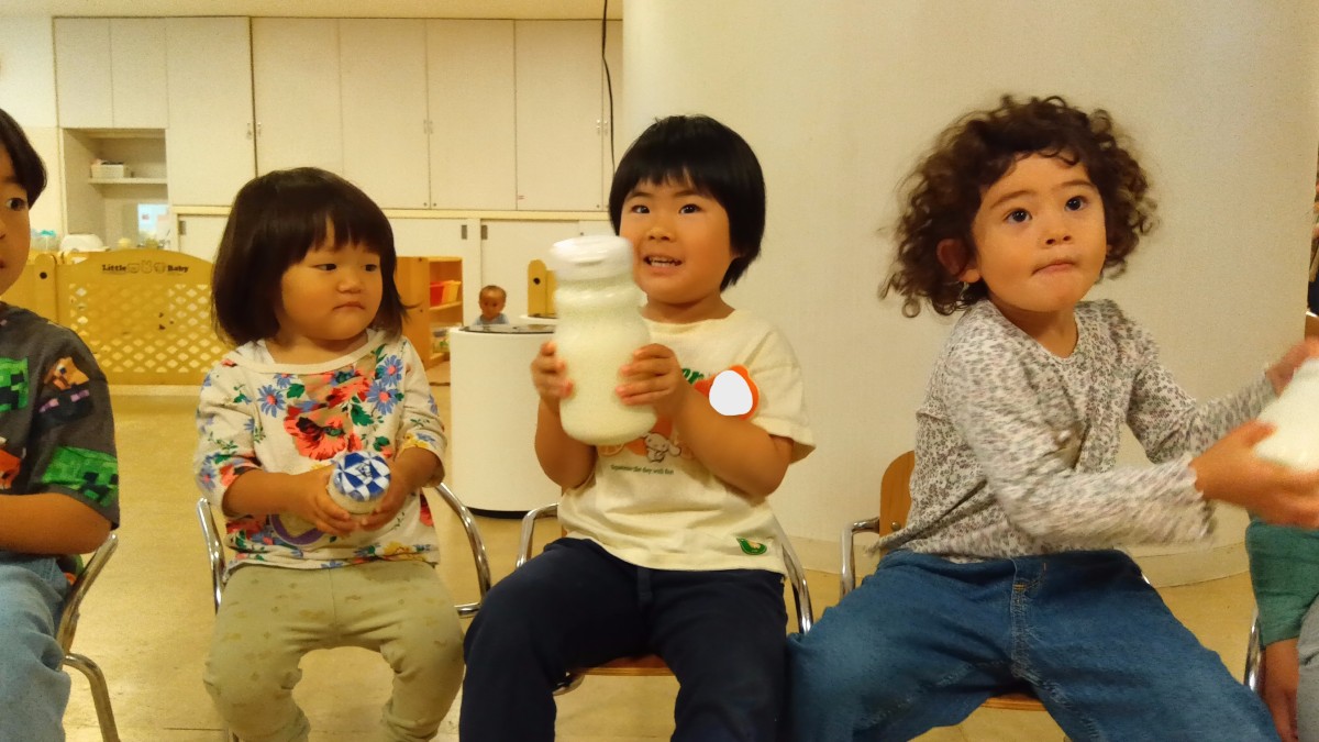 子どもたちは椅子に座り、瓶を振っている。
