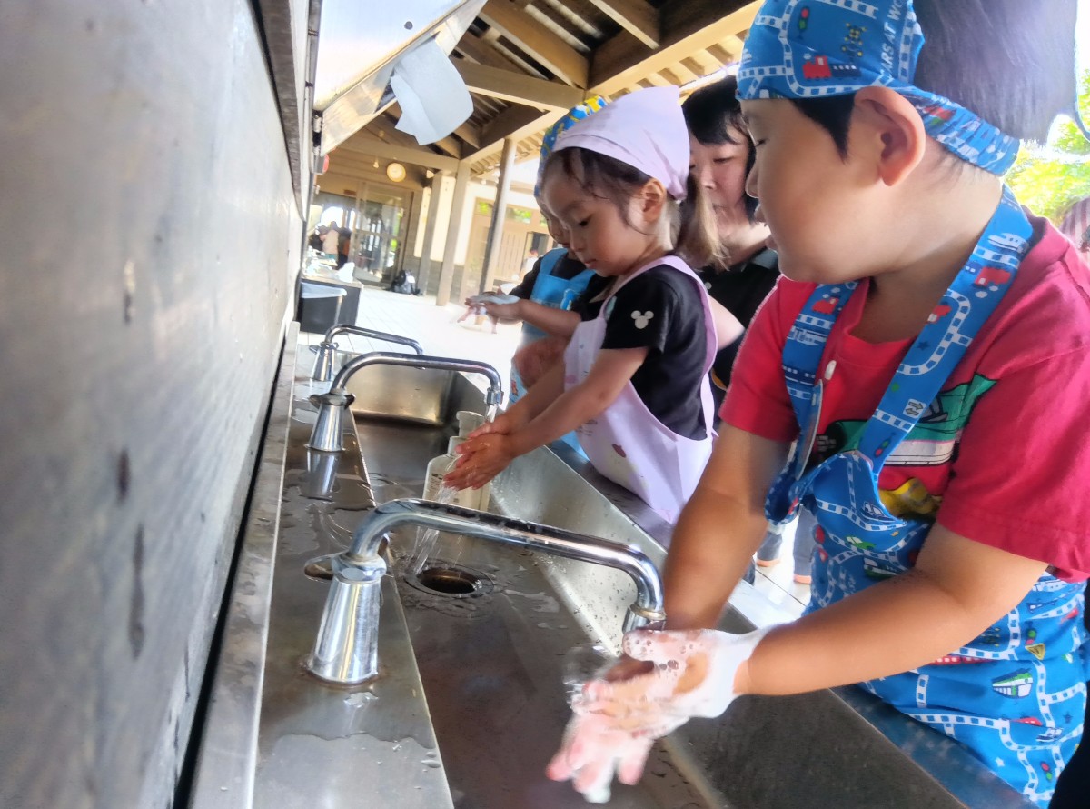 エプロンと三角巾を着けた子どもたちが水道場で手を洗っている
