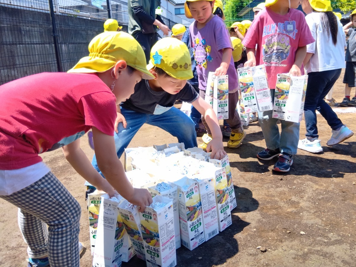 園庭で一列に並んでいる子どもたちは、肩を寄せ合ったり、手を握り合ったり、笑顔や心配そうな表情などを浮かべている。